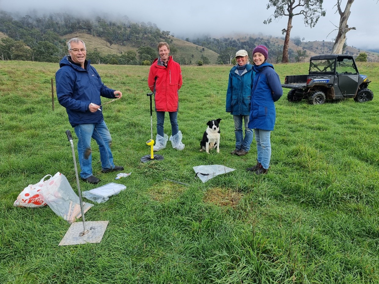 Four people and a border collie in a field with soil sample equipment
